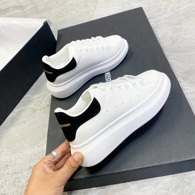 White sneakers with black accents on a gray surface, held by a hand.