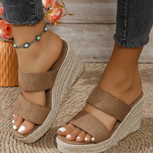 Beige wedge sandals worn with a floral arrangement in the background