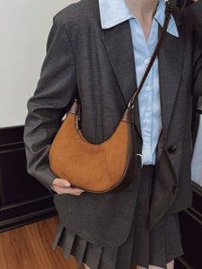 Brown leather handbag held by a person with a denim jacket in the background