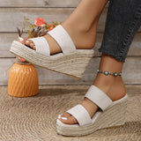 White wedge sandals worn with dark jeans on a wooden floor.