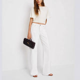 Woman wearing a white outfit with a black clutch against a white background