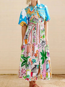 Woman wearing a colorful dress with a pattern of palm trees, animals, and abstract shapes.